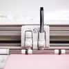 Close-up of a cutting machine's tool carriage with a pen inserted, over a pink sheet of material. Produktbild-Vorschau