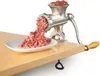 A manual meat grinder is shown attached to a wooden table, grinding meat into a white plate. Produktbild-Vorschau