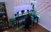 A gaming setup with dual monitors, a computer tower, and various decorative elements and figures. Produktbild-Vorschau