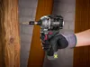 A person wearing a glove is using a cordless impact driver to screw a screw into a wooden beam. Produktbild-Vorschau