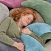 A young woman with red hair is sleeping comfortably, nestled among several large, plush pillows of various colors. Produktbild-Vorschau