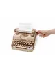 A wooden typewriter model with a piece of paper in it, and a hand turning a knob. Podgląd zdjęcia produktu
