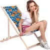 A woman sitting on a folding deck chair with a tropical orange pattern. Produktbild-Vorschau
