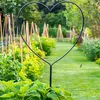 A heart-shaped garden stake stands in a lush garden with a pathway leading into the distance. Produktbild-Vorschau
