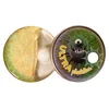 A glittery yellow substance in a clear plastic container, next to a round tin with a cartoon monster illustration and text. Podgląd zdjęcia produktu