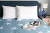 A bed with two white pillows and a blue star-patterned blanket, with a small tray of items on the blanket. Produktbild-Vorschau