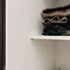 A close-up view of folded clothes on a shelf inside a closet. Produktbild-Vorschau