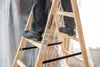 A person is standing on a wooden ladder, possibly during a renovation or painting job, with plastic sheeting in the background. Produktbild-Vorschau