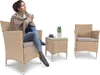 A woman sits in a wicker chair, wrapped in a blanket and holding a mug. A small table with a cake and a plant sits next to her, with another wicker chair to the right. Produktbild-Vorschau