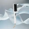 A white hair straightening brush is displayed against a backdrop of flowing white and light blue fabric. Produktbild-Vorschau