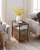 A side table with two drawers and a power strip sits between two chairs. A person is using a laptop in one chair, and another person is using a smartphone in the other chair. Náhled obrázku produktu