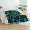 A dark green blanket with a Christmas pattern is draped over a white sofa. A small clock and a yellow book are on the blanket. Produktbild-Vorschau