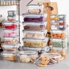 A collection of clear plastic food storage containers filled with various food items, neatly stacked on a countertop. Produktbild-Vorschau