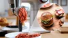 A kitchen appliance is shown grinding meat, with an inset image of a finished burger. Anteprima dell’immagine prodotto
