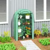 A green greenhouse with plants on shelves, placed next to a building with windows. Voir les images du produit