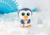 A plush penguin toy sitting on a snowy surface with decorative fans in the background. Produktbild-Vorschau