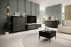 A modern living room with black furniture, including a credenza, TV stand, and coffee table, set against a muted green wall and a light-colored rug. Produktbild-Vorschau
