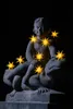 A stone statue of a child sitting on a frog, decorated with glowing star-shaped lights. Produktbild-Vorschau