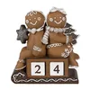A decorative Christmas figurine of two gingerbread people sitting on a sled with a calendar block showing '24'. Produktbild-Vorschau