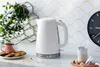 A white Russell Hobbs kettle is displayed on a countertop with a cup of tea and cookies. Produktbild-Vorschau
