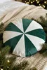 A round pillow with green and white stripes is placed on a cream-colored knitted blanket, surrounded by pine branches and fairy lights. Podgląd zdjęcia produktu