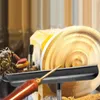 A close-up view of a woodturning tool rest with a wooden handle, positioned in front of a wood lathe and a piece of wood being shaped. Náhled obrázku produktu