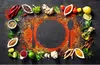 A flat lay of various spices, herbs, and ingredients arranged around a dark circular surface, with a fork and spoon silhouette. Produktbild-Vorschau