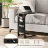 A side table with integrated charging ports and storage pockets is placed next to a sofa, with a laptop and coffee cup on top. Produktbild-Vorschau