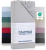 A stack of folded fitted sheets in various colors, with a close-up of a grey fitted sheet in the foreground. The grey sheet has a label with brand and product information. Produktbild-Vorschau