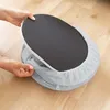 Hands are shown adjusting a gray foot warmer with a black textured sole on a wooden floor. Produktbild-Vorschau