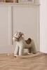 A plush rocking horse with a striped pattern sits on a wooden floor in front of a white paneled wall. Produktbild-Vorschau