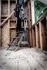 A person standing on a step stool holding a power tool inside a building under construction. Anteprima dell’immagine prodotto