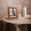 A wooden photo frame is placed on a round table covered with a brown tablecloth, next to a vase with branches. Podgląd zdjęcia produktu