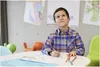 A young boy is drawing at a table with colorful drawings on the wall behind him. Anteprima dell’immagine prodotto
