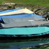 Several boats covered with protective tarps are lined up on the water's edge, with a grassy embankment in the background. Produktbild-Vorschau
