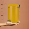 A hand is holding a yellow pedal trash can next to a ruler showing measurements in centimeters. Voir les images du produit