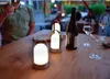 Three LED lanterns and a wine bottle are on a wooden table, with a person in the background holding a glass. Produktbild-Vorschau