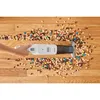 A hand is holding a white handheld vacuum cleaner on a wooden floor, cleaning up a spill of nuts and candies. Produktbild-Vorschau