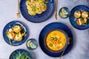 A table setting with various dishes, including soup, ravioli, and small tarts, along with drinks. Voir les images du produit