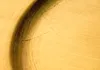 A close-up macro shot of a textured gold surface with a dark curved line and fine cracks. Produktbild-Vorschau