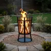 A fire pit with a flame is placed in a garden setting on a stone patio with gravel and plants. Anteprima dell’immagine prodotto