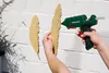 A person is using a hot glue gun to attach a feather-shaped object to a white brick wall. Produktbild-Vorschau