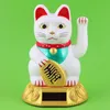 A white lucky cat figurine with a gold coin and a solar panel base, set against a green background. Produktbild-Vorschau