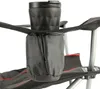 A close-up view of a black fabric cup holder attached to the armrest of a camping chair, with a black travel mug inside. Náhled obrázku produktu