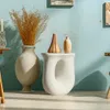 A close-up studio shot of a modern sculptural side table with two decorative vases and dried grasses. Náhled obrázku produktu