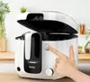 A hand is pressing a button on a white and black deep fryer, which is open, on a kitchen counter. Produktbild-Vorschau