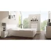 A modern bedroom with a white bed, nightstands, and a dresser, featuring large windows with a view of trees. Voir les images du produit