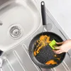 A hand is cleaning a dirty frying pan with a green sponge next to a kitchen sink. Náhled obrázku produktu
