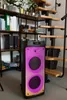 A portable Bluetooth speaker with colorful lights is placed on the floor next to a spiral staircase and shelves filled with books and plants. Náhľad obrázku produktu