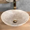 A close-up view of a beige stone basin with a gold drain and faucet, set on a wooden surface. Náhľad obrázku produktu